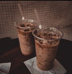 two iced coffee drinks sitting on top of a wooden table