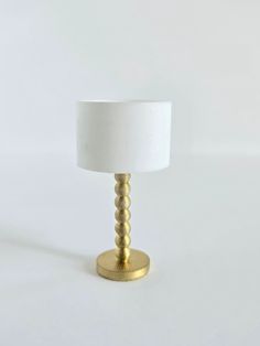 a white lamp sitting on top of a table next to a white light bulb and a gold plated base