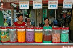 two women standing behind a counter filled with different types of condiments and drinks