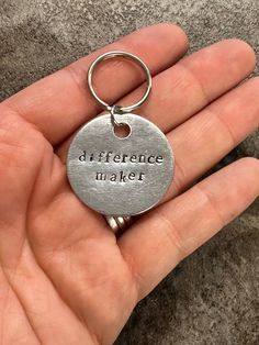 a hand holding a metal keychain that says, diffrentce maker