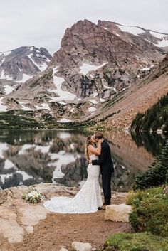 a bride and groom kissing in front of a mountain lake with snow on the mountains