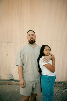 a man and woman standing next to each other in front of a building with a wall behind them