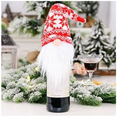 a wine bottle with a red and white knitted gnome hat on it next to christmas decorations