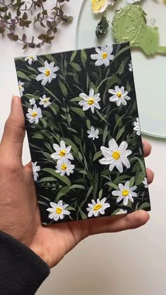 a hand holding up a black and white card with daisies painted on the front