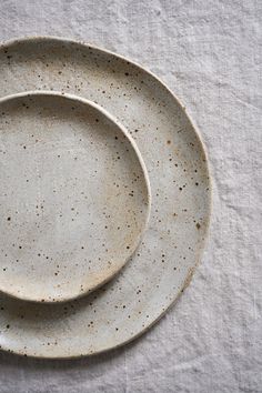 two white plates with speckles on them sitting on a tableclothed surface