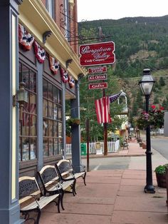 an empty bench on the sidewalk in front of a store with flags hanging from it's windows