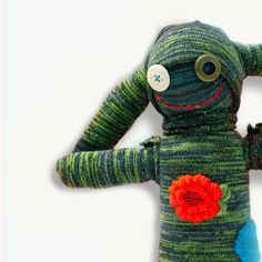 a knitted toy with an orange flower on it's head and arms, sitting in front of a white background