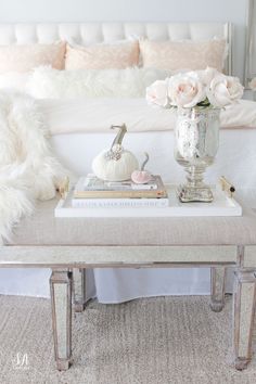 a white bed sitting next to a table with books on it and flowers in a vase