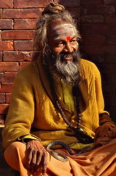 an old man sitting on the ground in front of a brick wall with his eyes closed