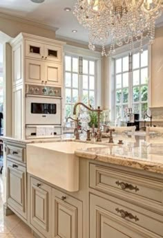 a large kitchen with marble counter tops and white cabinets, chandelier hanging from the ceiling