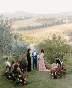 a group of people sitting on top of a lush green field next to trees and flowers