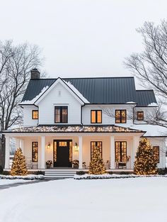 a large white house with christmas lights on the windows and trees in front of it