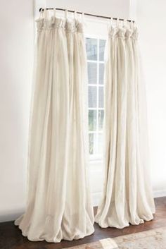 a white curtain hanging in front of a window next to a rug on top of a wooden floor