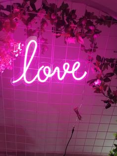 a pink neon sign that says love hanging from the side of a wall next to a plant