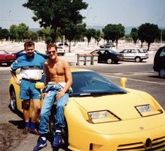 two men sitting on the hood of a yellow sports car in front of a parking lot