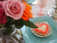 a vase filled with pink roses next to a heart shaped cookie on a blue plate