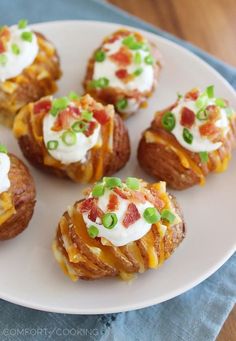 mini potatoes with bacon, cheese and green onions on a white plate next to a blue napkin