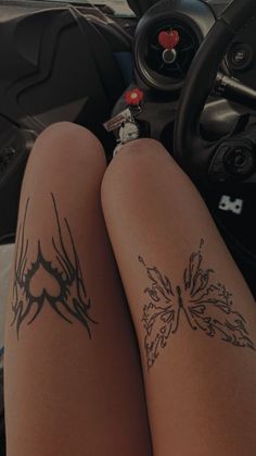 a person with tattoos on their legs sitting in a car next to a steering wheel