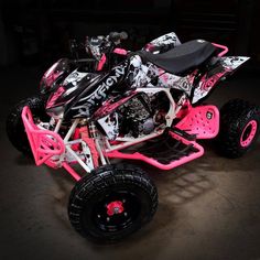 a pink and black toy atv is parked in the dark with its wheels out,