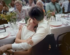 a man and woman hugging each other at a dinner table