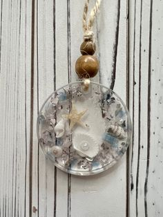 a clock made out of glass and shells hanging on a white wooden wall with rope