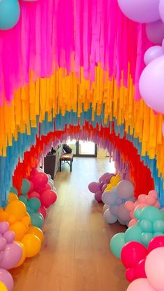 colorful balloons and streamers are hanging from the ceiling in an indoor space with wood flooring