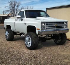 a white pickup truck parked in front of a building with large tires on it's rims