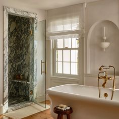 a bath tub sitting next to a window in a white bathroom with marbled walls