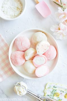 pink and white marshmallows are in a bowl next to some spoons