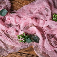 pink sheer fabric with green leaves on wooden table top, closeup view from above