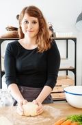 a woman standing in front of a cutting board with vegetables on it and a bowl next to her