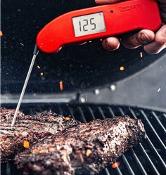 a person is grilling steak on the grill with an electronic thermometer in their hand