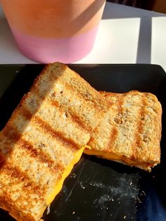 two pieces of grilled cheese sit on a black plate next to a pink cup