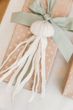 a gift wrapped in brown paper with a green ribbon and a white tassel hanging from it