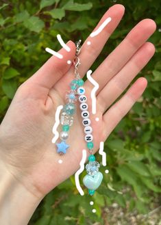 someone is holding their hand with some beads and charms on it in front of green leaves