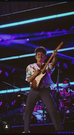 a young man playing an electric guitar in front of purple and blue lights on stage