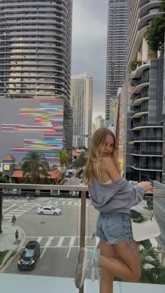 a woman standing on top of a balcony next to tall buildings and looking at the camera