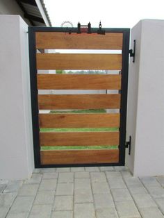 an open wooden gate on the side of a house with brick walkway and white walls