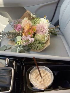 flowers are sitting on the dashboard of a car, next to a drink in a plastic cup