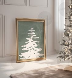 a white christmas tree sitting in front of a window next to a framed poster on the wall