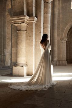 a woman in a wedding dress is looking at the light coming through an arched building