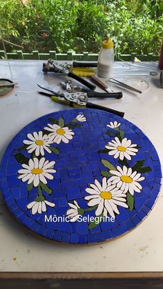 a blue plate with white daisies on it sitting on a table next to paintbrushes