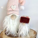 two white and red gnomes sitting on top of a piece of wood