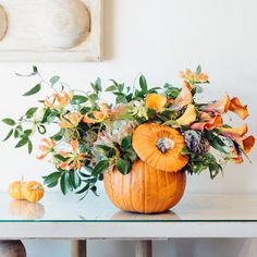 an arrangement of flowers and pumpkins on a table