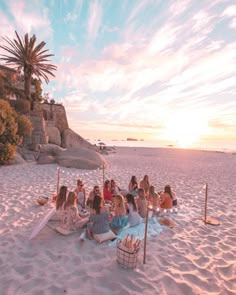 a group of people sitting on top of a sandy beach next to the ocean at sunset