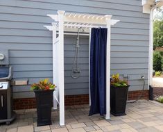 an outdoor shower with blue curtains and potted plants on the side of a house