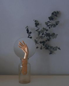 a person's hand reaching out from behind a glass vase with flowers in it