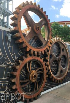 two large metal gears sitting next to each other on a black and white wall with blue sky in the background