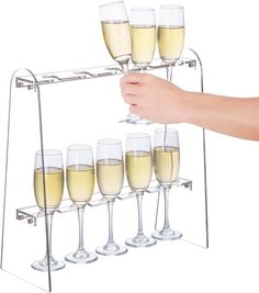 a hand is holding a rack with wine glasses on it and five champagne flutes in the bottom