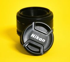 a camera lens cap with the nikon logo on it sitting in front of a yellow background